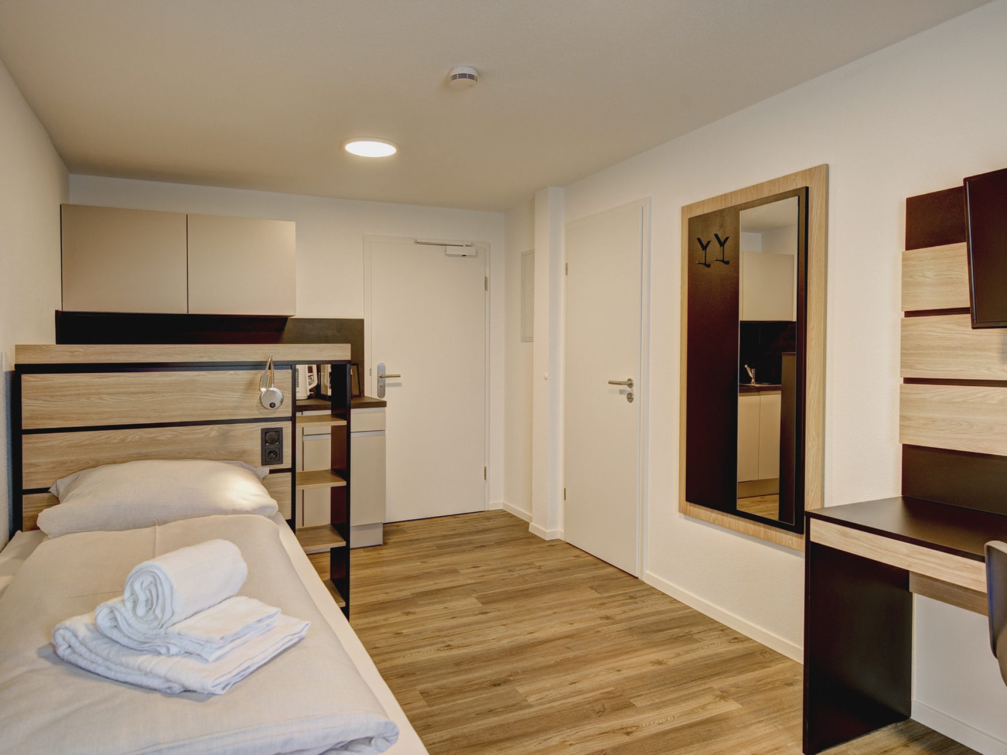 Schönes Apartmentzimmer mit Einzelbett, Küchenzeile hinter dem Bett, Arbeitsbereich, Schrank und Garderobe