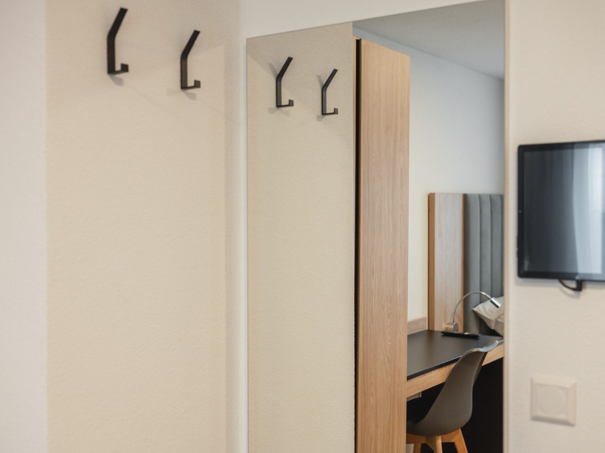 Details der Garderobe mit Kleiderhaken und Spiegel mit Spiegelung vom Arbeitsbereich und Bett. Tablet für die Smart Home Steuerung hängt an der Wand.